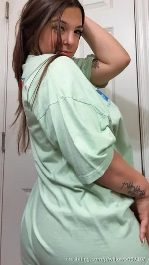 Woman in oversized green t-shirt, posing indoors near door, tattoos on arms.
