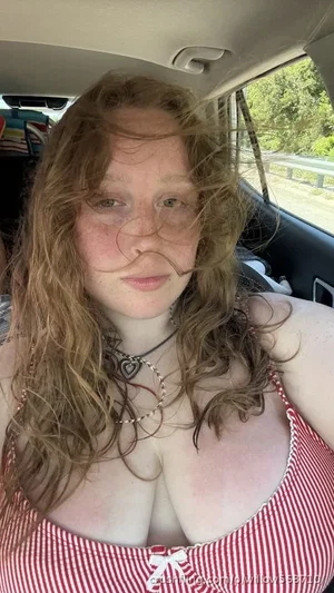 Woman with curly hair in red and white striped top sitting in car.