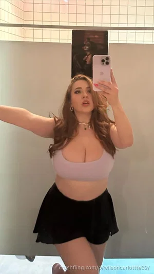 Woman in lavender crop top and black skirt poses in mirror selfie, indoor setting.