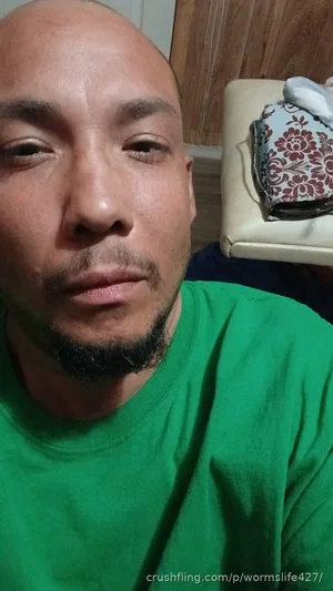Man with shaved head and beard wearing green shirt indoors.