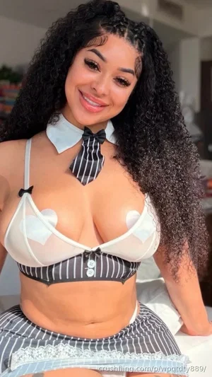 Woman with curly hair in a striped schoolgirl outfit with sheer white bra, indoors.