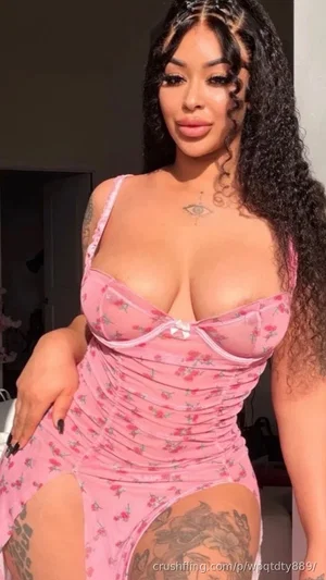Woman in pink floral lingerie with tattoos, posing indoors.