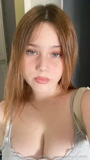Woman with light brown hair and blue eyes wearing a gray lace tank top, indoor selfie.