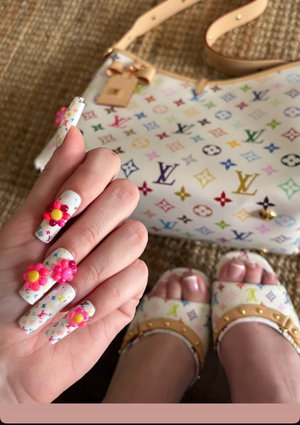 Woman's hand with floral nail art, matching sandals, and a colorful patterned handbag on a textured