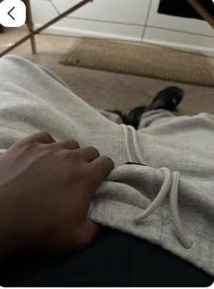 Person in gray sweatpants and black shoes, sitting indoors, hand resting on lap.