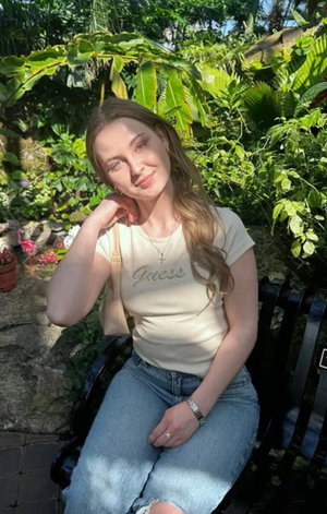Woman with long hair in t-shirt and jeans sitting outdoors.