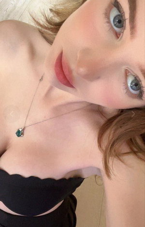 Reddish-haired woman in black top and necklace taking selfie.