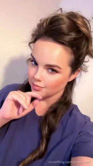 Woman with styled brown hair in a blue top, posing indoors.