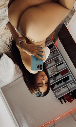 Woman in white lingerie taking mirror selfie in bedroom with shoe rack visible.