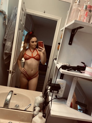 Woman in red lingerie taking mirror selfie in bathroom.