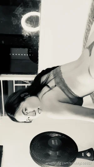 Woman in black lace lingerie lying on bed, indoor setting with fan and mirror.