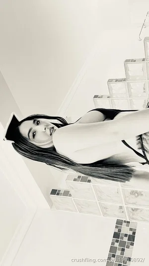 Woman with long dark hair in black lingerie posing on tiled stairs indoors.