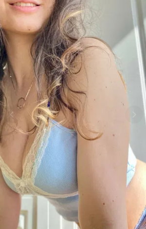 Woman with long wavy hair wearing blue lace bra indoors.