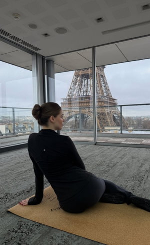 Woman in black athletic wear on yoga mat with Eiffel Tower view.