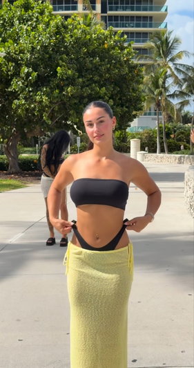 Woman in black top and yellow towel outdoors on paved path.