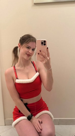 Woman in red Santa outfit taking mirror selfie indoors.