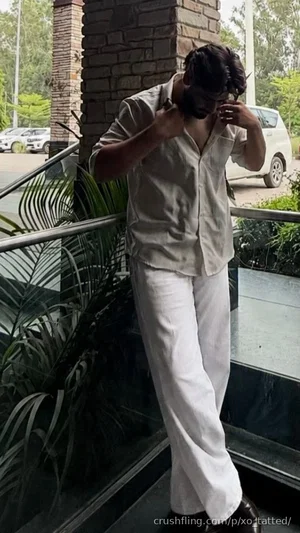Man in light shirt and white pants adjusting mask outdoors near plants and railing.