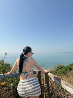 Brunette woman in bikini top and skirt overlooking ocean.