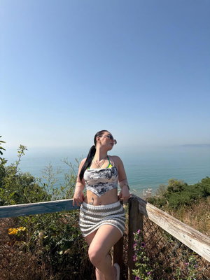 Asian woman in crop top and skirt posing by ocean railing.