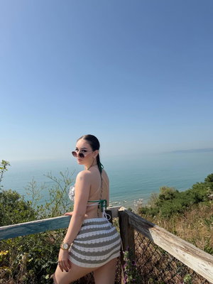 Woman in bikini top and striped skirt at ocean overlook.