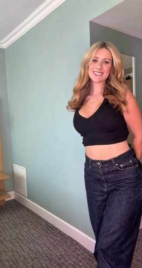 Blonde woman in black crop top and jeans posing indoors.