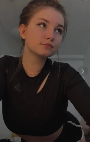 Woman with light brown hair in black crop top taking selfie indoors.