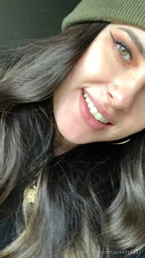 Woman with long dark hair and green beanie smiling in close-up selfie.