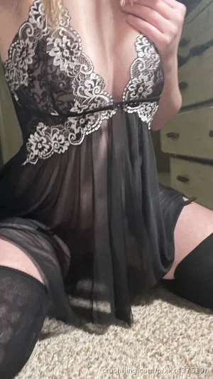 Woman in black lace lingerie and stockings kneeling on carpet indoors.