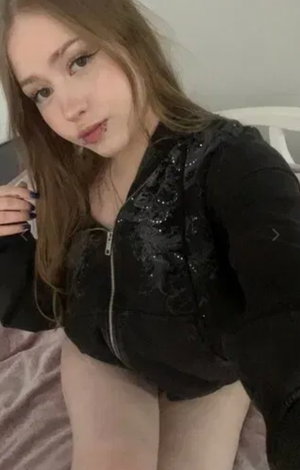Woman with long brown hair in black jacket on bed.