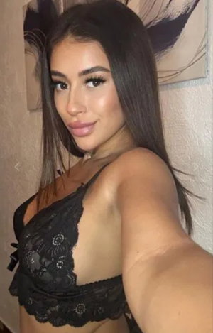 Woman with long dark hair wearing black lace bra takes indoor selfie.