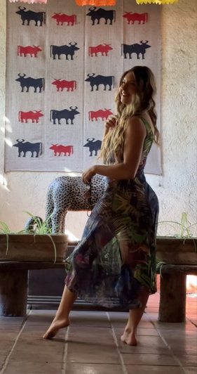 Blonde woman in floral dress sitting on bench indoors.