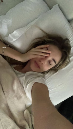Woman in white t-shirt lying in bed taking selfie.