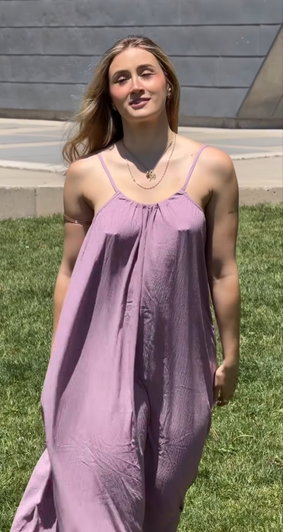 Woman in lavender dress standing on grass outdoors, long hair, smiling.