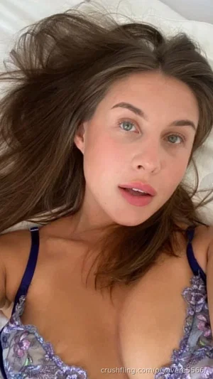 Woman with brown hair and green eyes lying on bed, wearing floral lace lingerie.