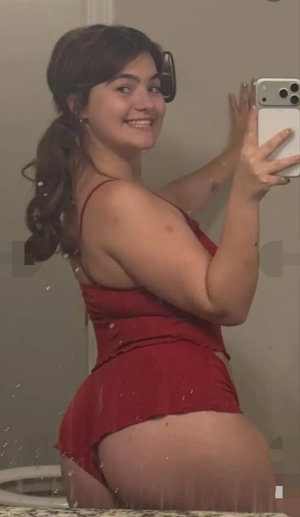 Woman in red dress taking mirror selfie in bathroom, wet hair, smiling.