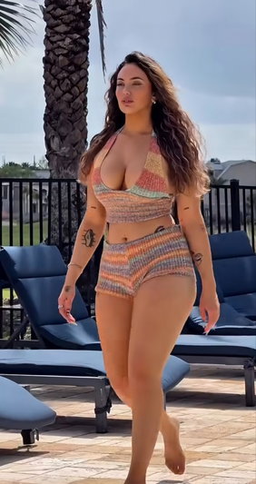 Woman in colorful knit bikini walking on patio near lounge chairs and palm tree.