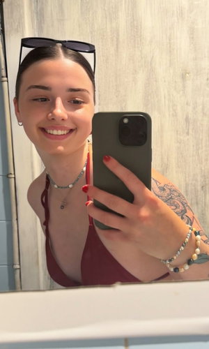 Woman in red top with tattoo on arm, smiling in mirror selfie.