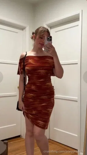 Woman in off-shoulder dress taking mirror selfie indoors.