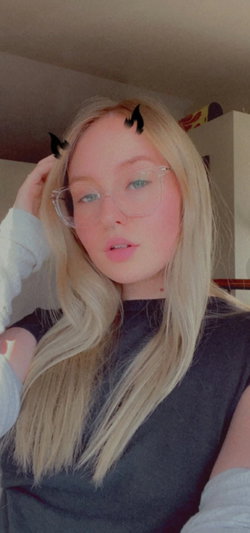 Blonde woman with glasses wearing dark top indoors.