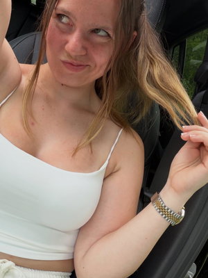 Woman with light brown hair in white top taking selfie in car.