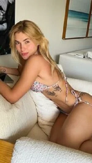 Blonde woman in floral bikini posing on white couch indoors.