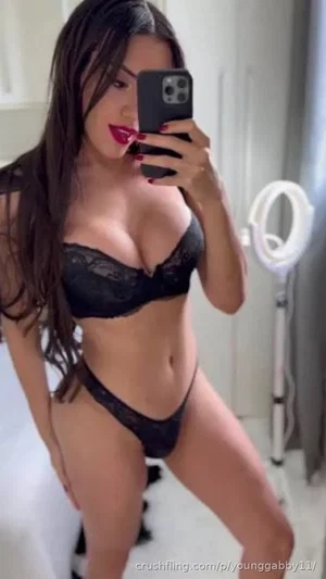 Woman in black lace lingerie taking mirror selfie in bathroom.