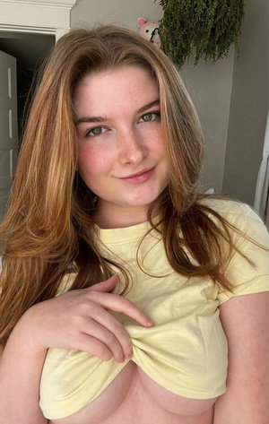 Woman with long auburn hair and freckles in yellow top indoors.