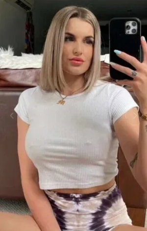 Blonde woman in white crop top taking selfie indoors.