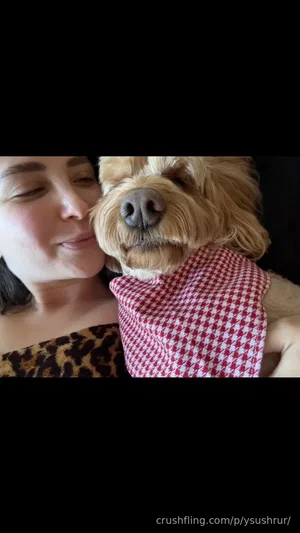 Woman in leopard print top hugging a dog wearing a red checkered bandana indoors.