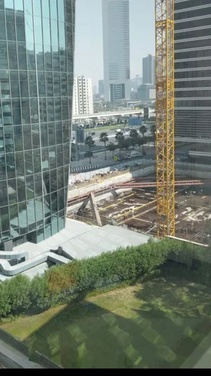 Cityscape with tall buildings, construction site, and greenery in foreground.