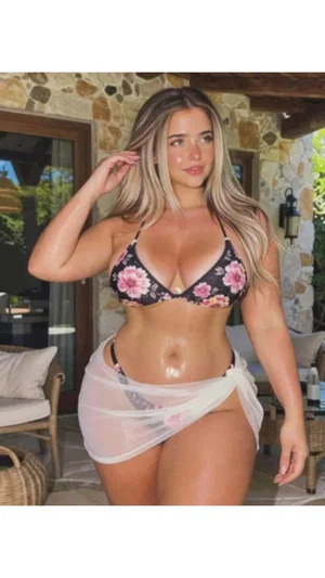 Woman in floral bikini top and sheer wrap, standing on patio with stone wall.