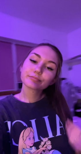 Woman with long hair wearing a dark graphic t-shirt indoors under purple lighting.